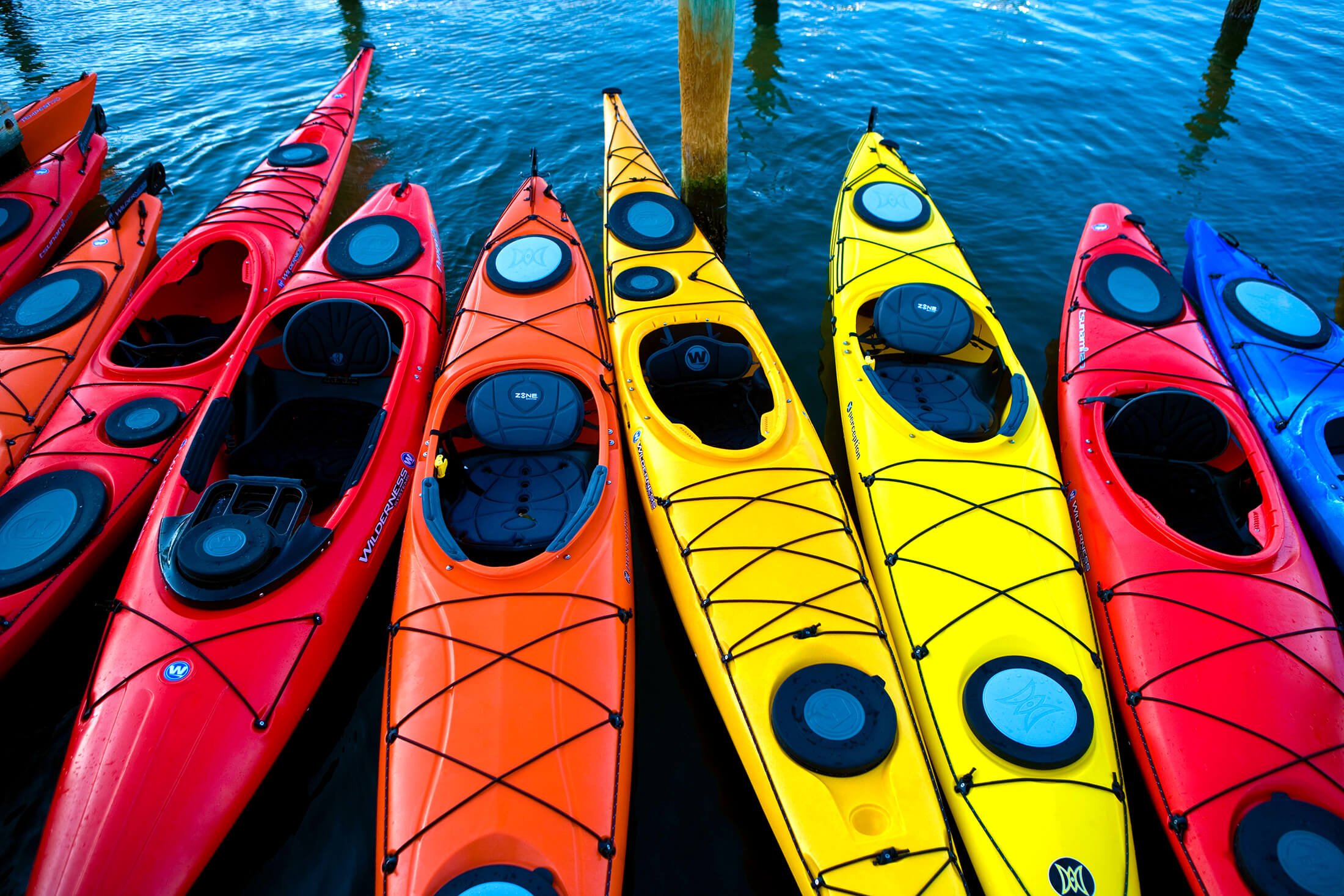 Kayaks of many colors float empty in the water.