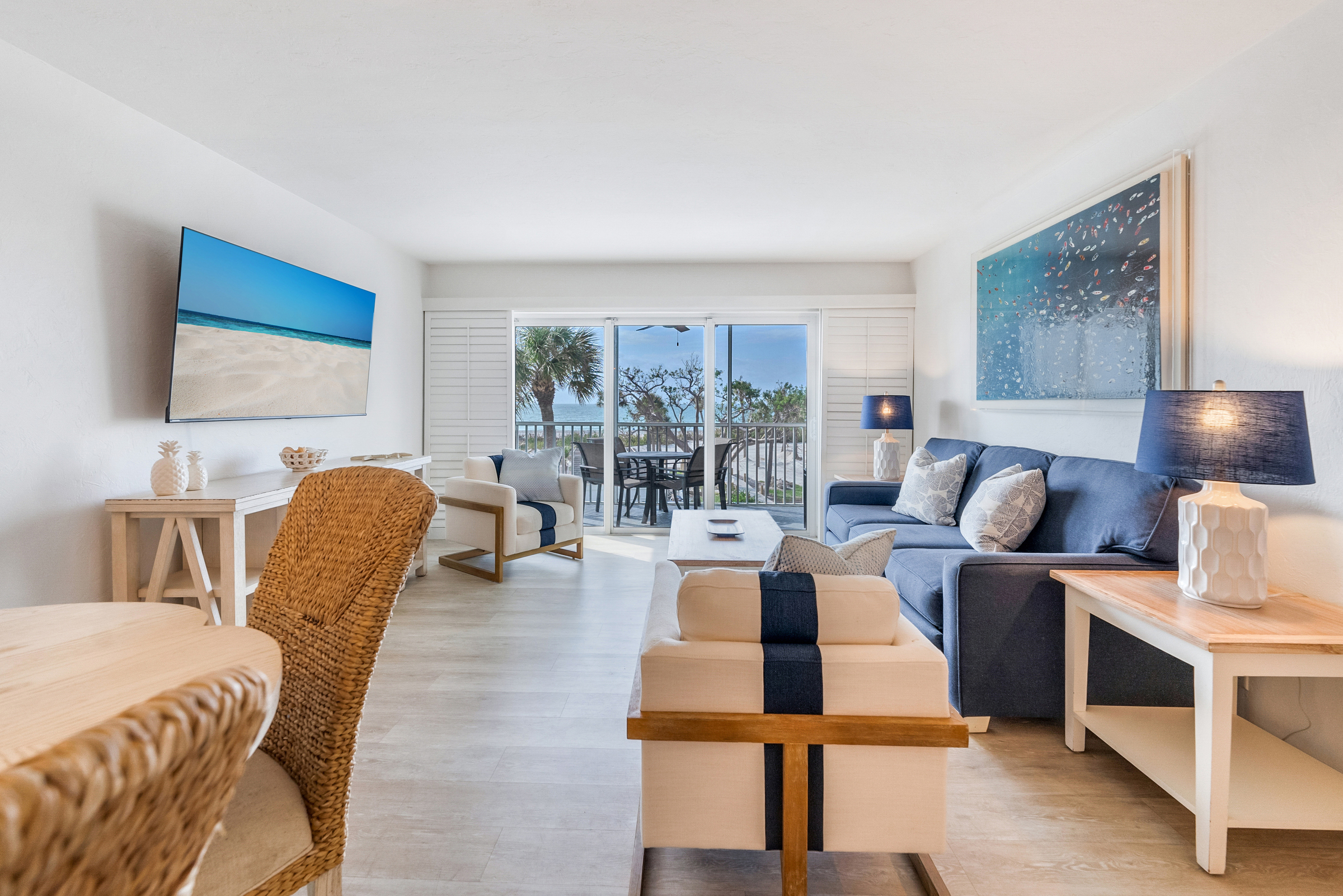 Couch and chairs in living room, TV on wall, view of balcony with palm trees