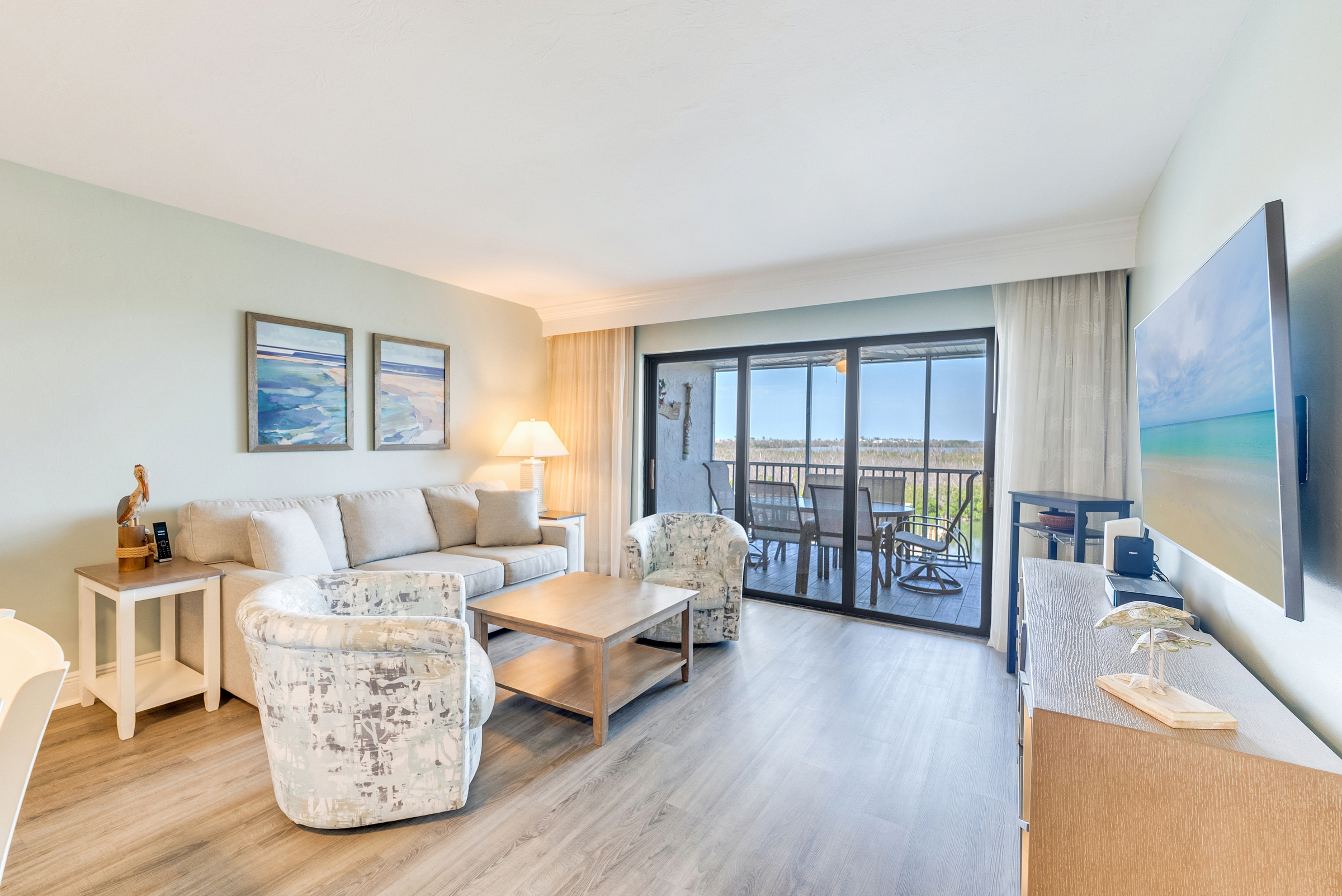 Living room with plush seating, wood floors, and a balcony view of the ocean.