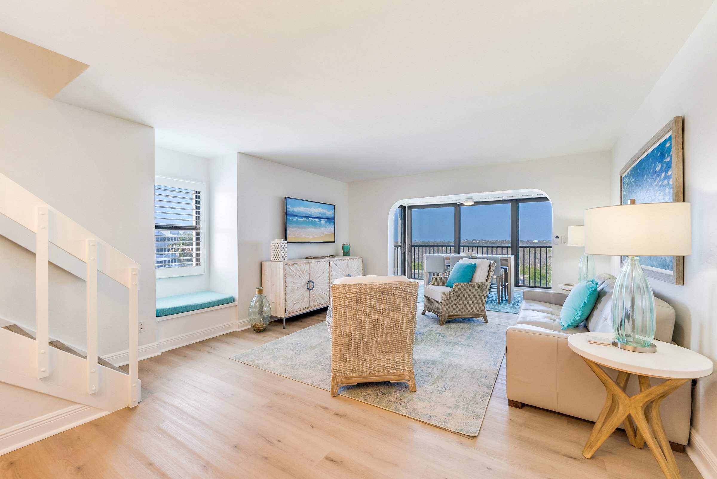 Living room with sofa, two chairs, TV stand, window seat, and sliding door to balcony