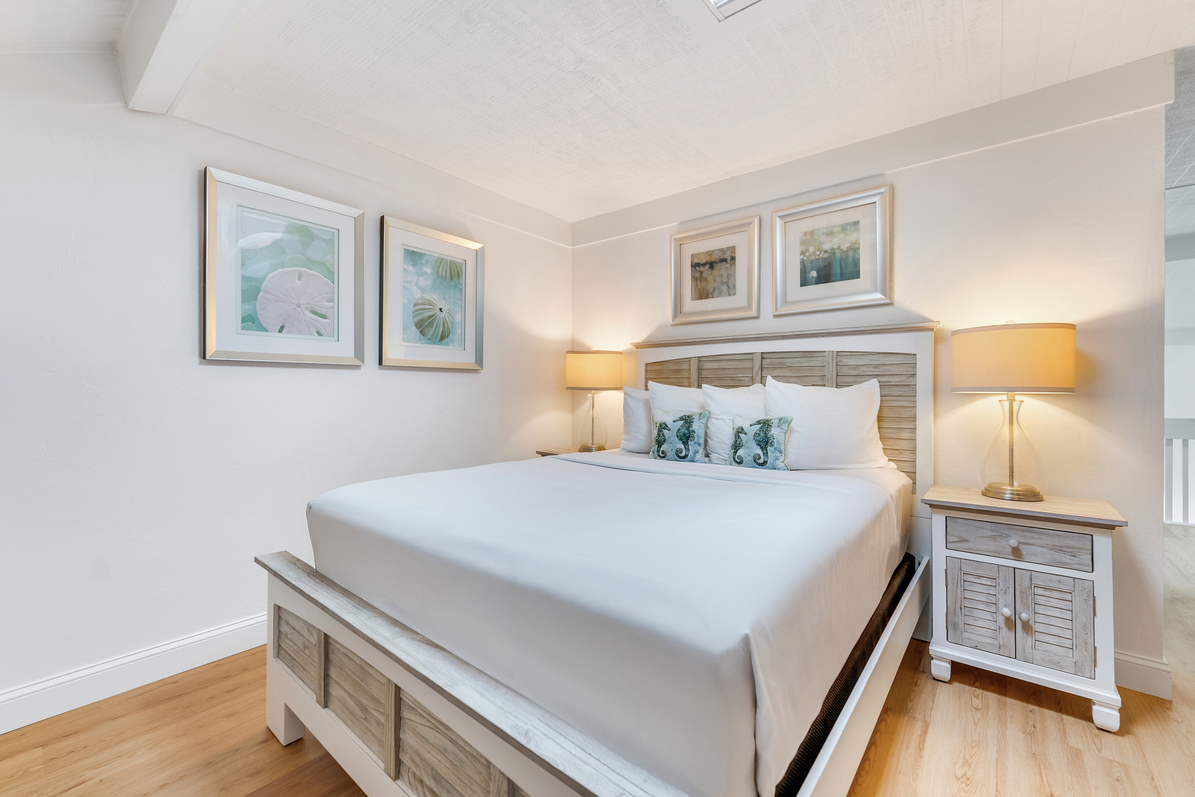 Bed with white bedding, two nightstands with lamps, and framed pictures on the wall.
