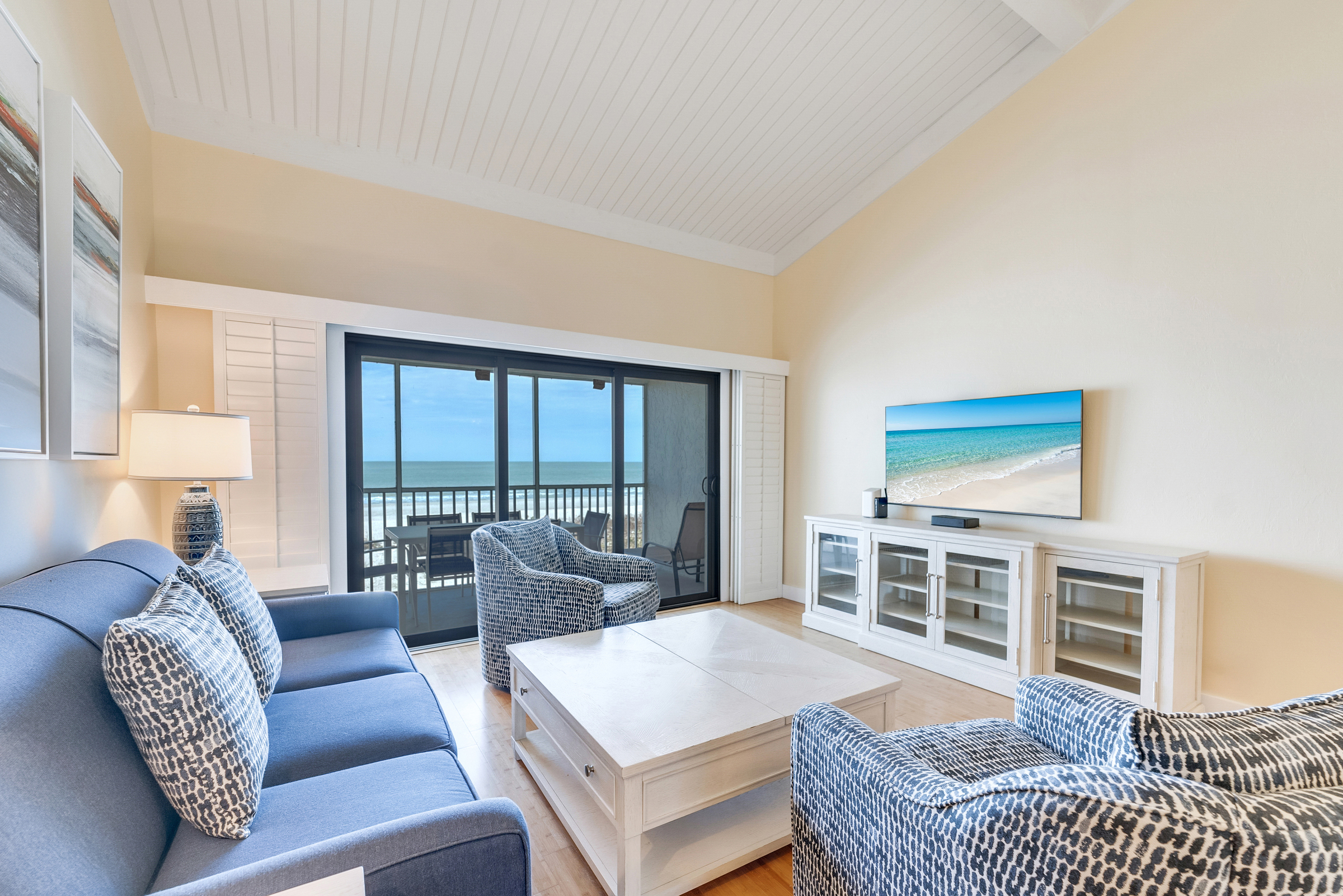 Living room with blue couch, armchairs, TV, and balcony view.