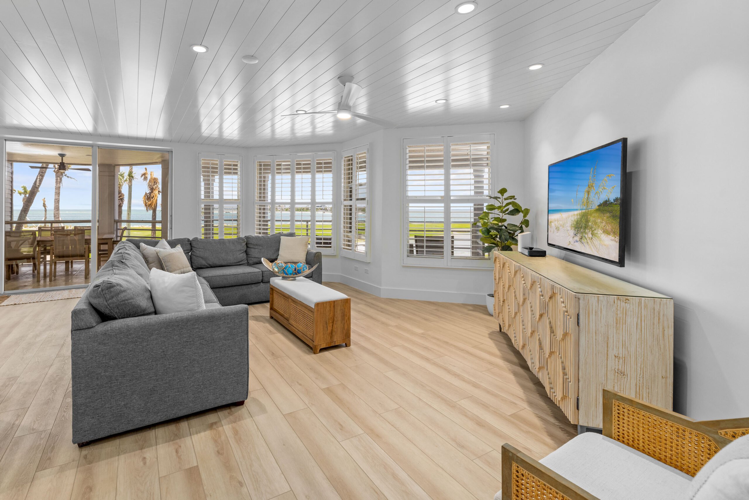 Living room with gray couch, wooden floors, and large windows showing ocean view