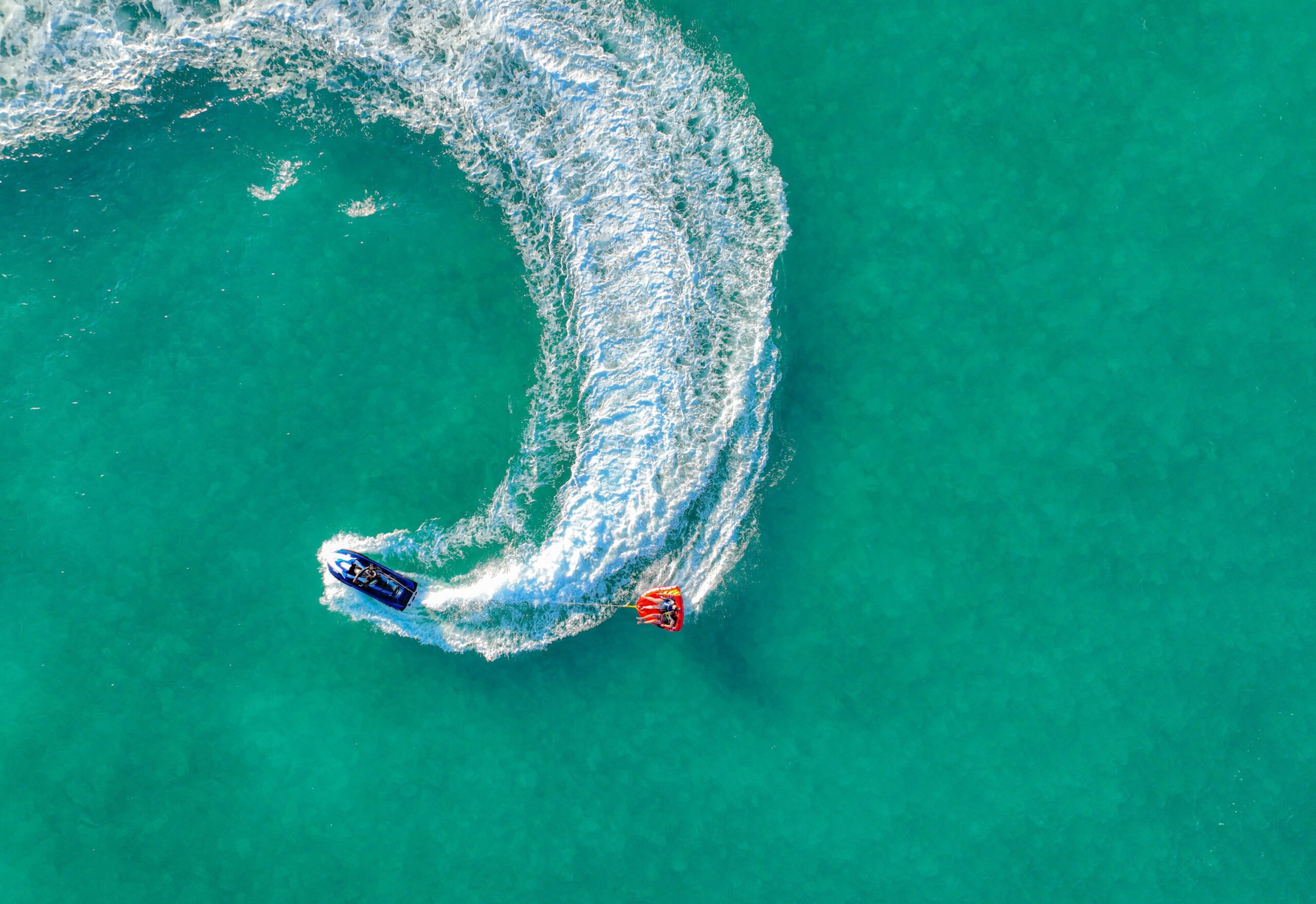 Aerial view of a boat towing a tube on turquoise water