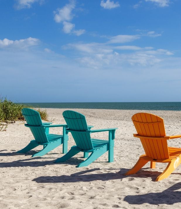 Three wooden beach chairs on sand facing the ocean