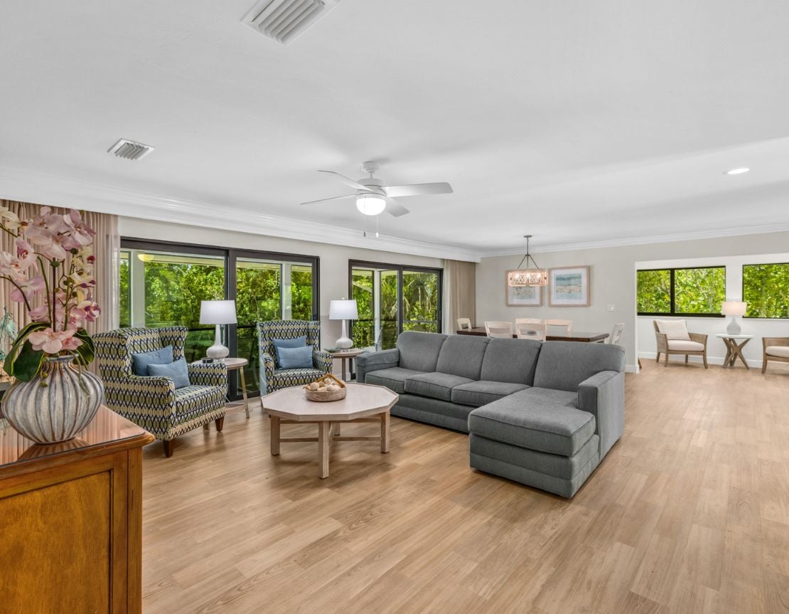 Living room with grey sectional, armchairs, and large windows with garden view