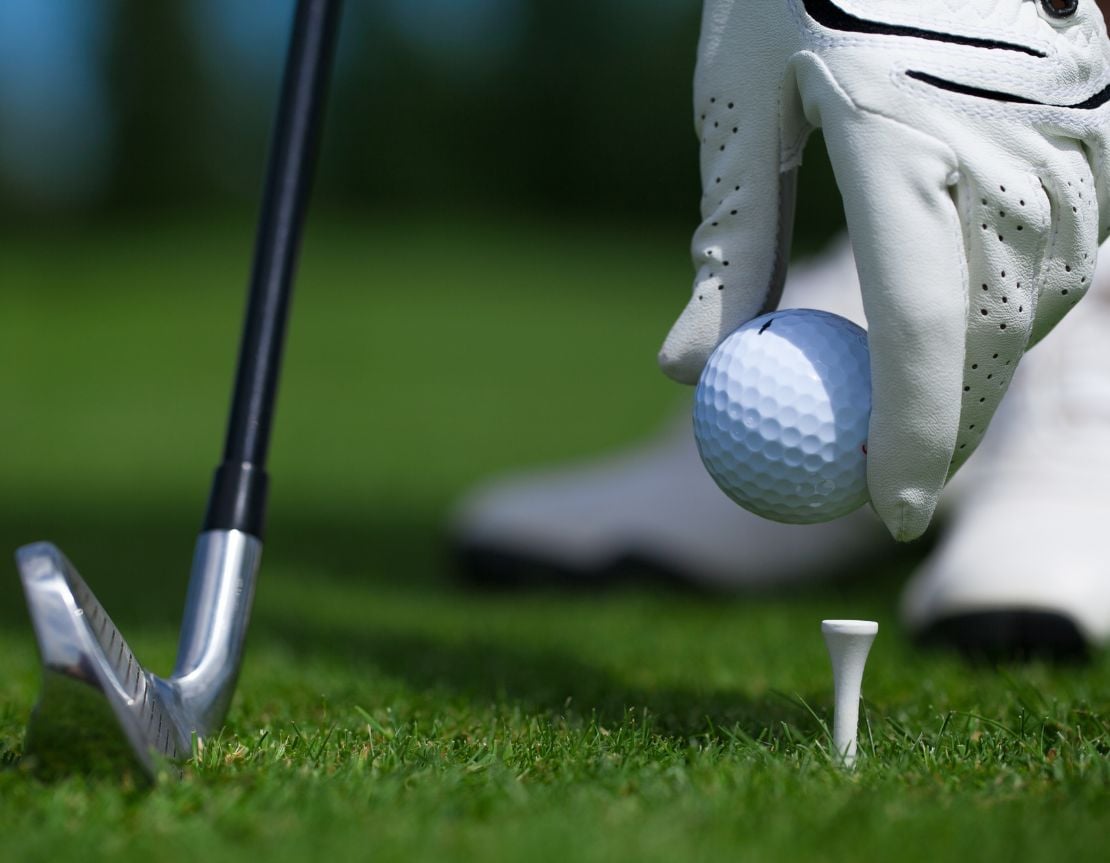 Golfer placing ball on tee with club ready
