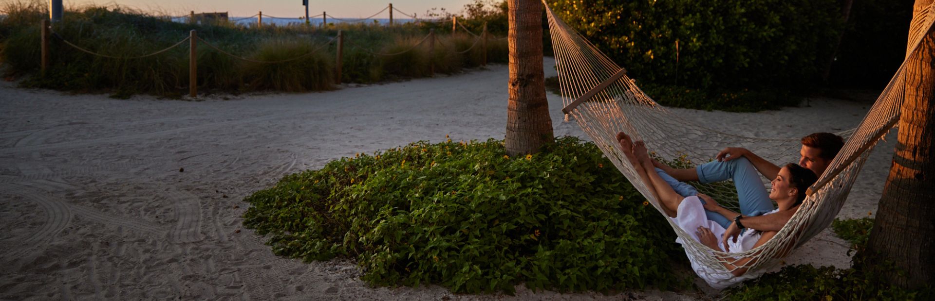 Two people relaxing in a hammock by the beach at sunset